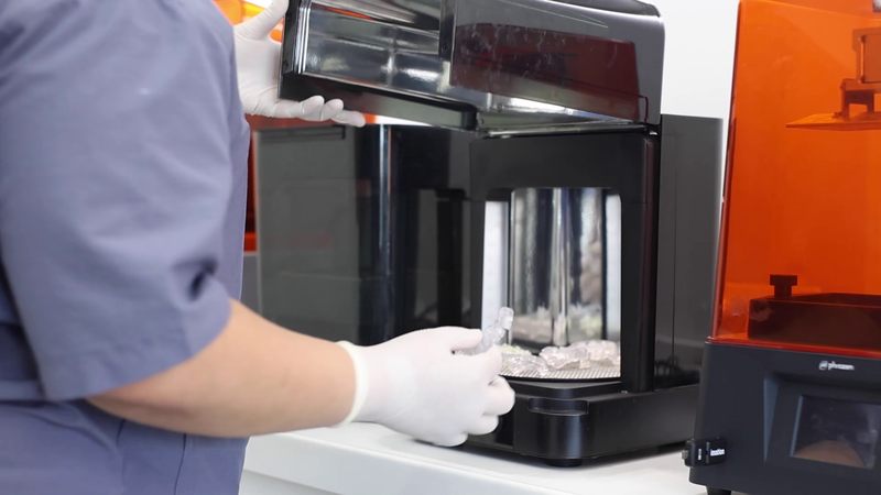 A printed surgical guide being lifted out of the clinic's 3D printer